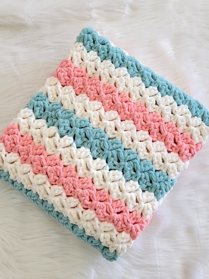 Fast crochet blanket pattern finished in peach, blue and cream colors folded neatly