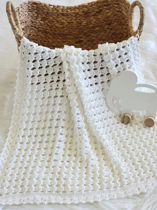 White gender neutral crochet baby blanket in a basket with an elephant toy