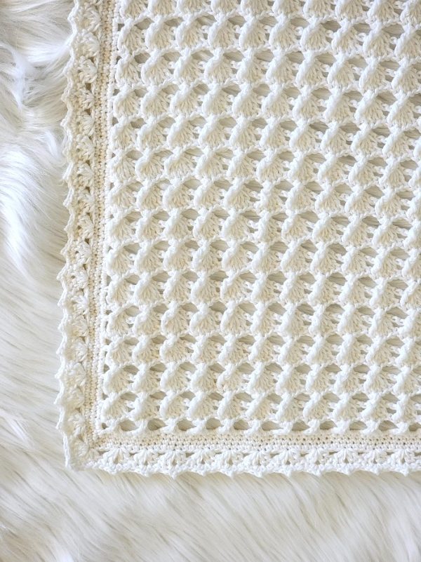 Closeup of the corner of white gender neutral blanket showing stitch pattern and border