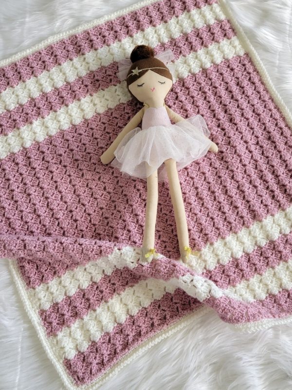 Crochet blanket in pink and cream color with a ballerina doll lying on it