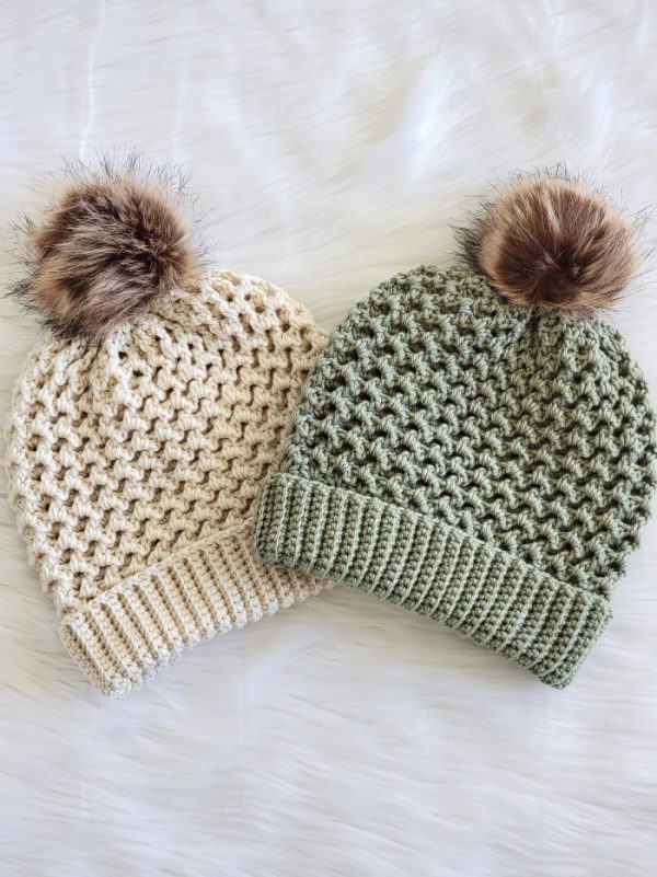 A pair of adult crochet hats finished in green and cream placed side by side