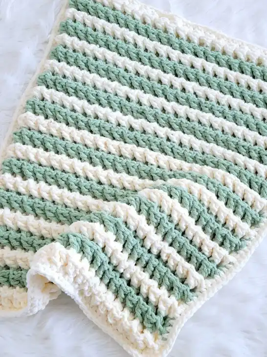 Chunky crochet blanket with green and cream colored stripes