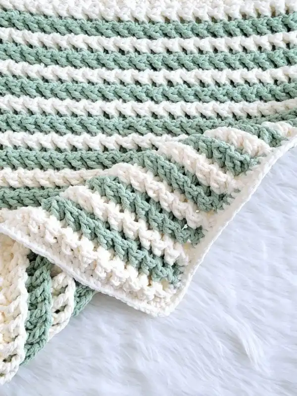 Corner of crochet blanket with green and cream color stripes