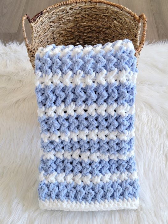 Blue crochet blanket displayed in a basket on white fur fabric