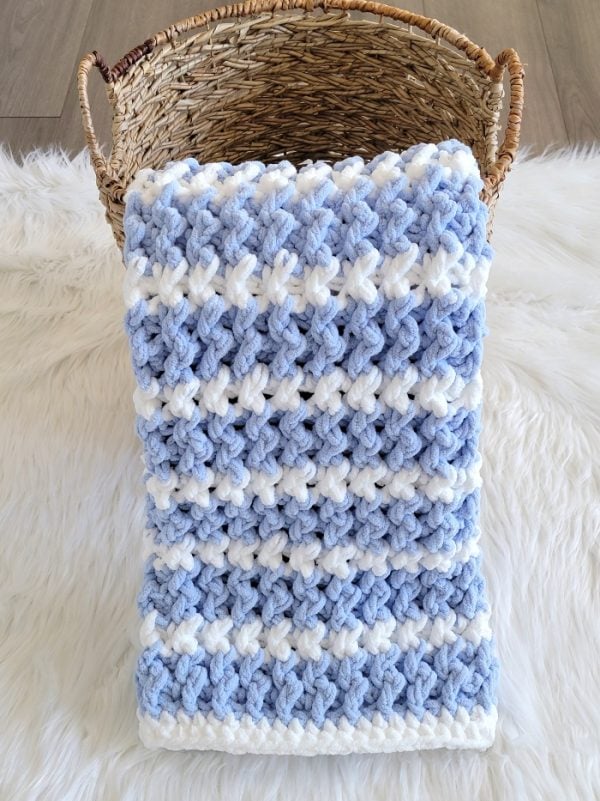 Blue crochet blanket displayed in a basket on white fur fabric