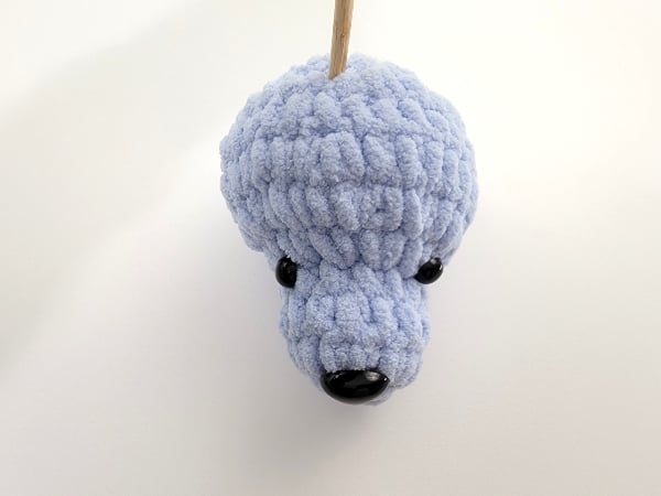 Head of crochet dog lovey in blue color held with a skewer