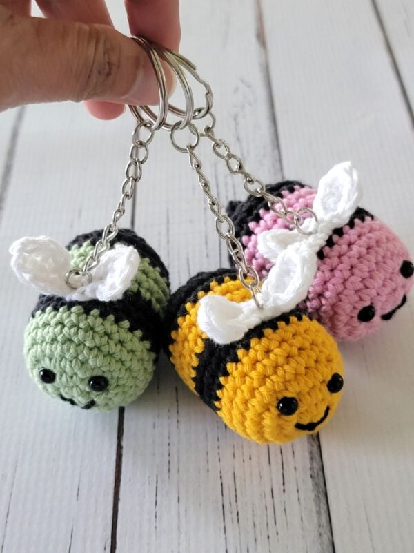 3 bee crochet keychains in pin, green and yellow held in hand