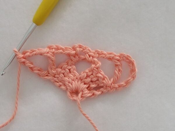 Row 2 of the crochet bandana with 2 V-titches connected by chain spaces, beginning to form the triangular shape.