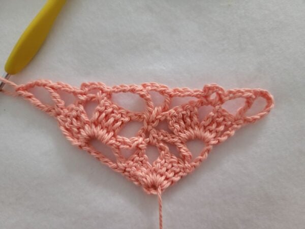 Row 4 of the crochet bandana with additional shell stitches and chain spaces, expanding the triangle evenly.