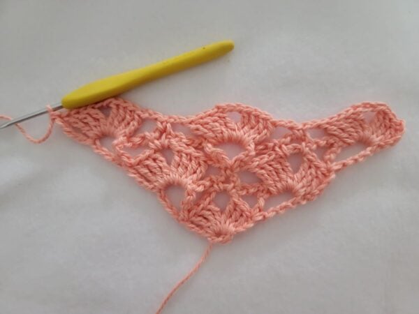 Row 5 of the crochet bandana featuring a wider lace triangle with repeating shell stitch motifs.