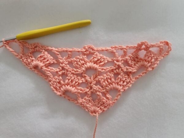 Row 6 of the crochet bandana showing the growing triangle with open chain spaces and more V-stitches.