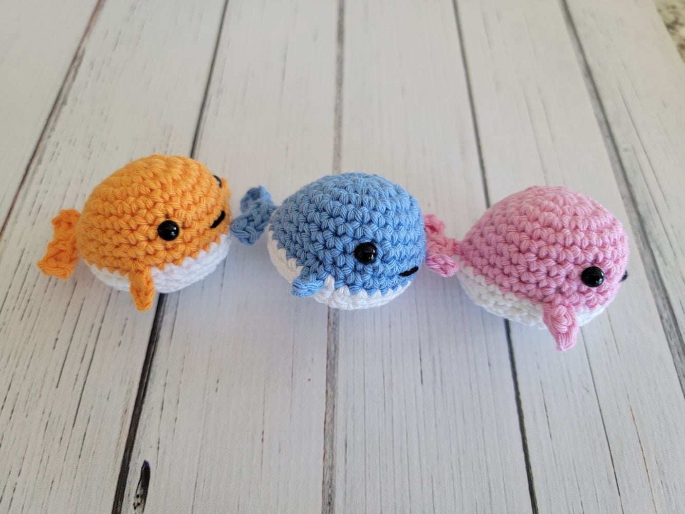 Tiny crochet whales in orange, blue and pink colors