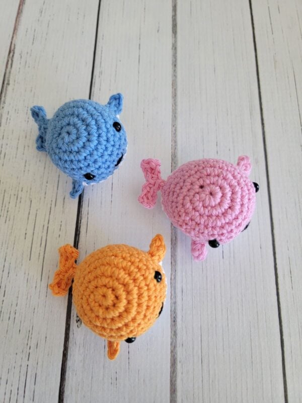 Top view of three tiny crochet whale plushies on a white wood background.