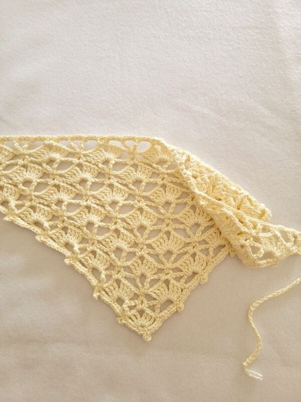 Cream handmade crochet head bandana folded to show the lightweight lace shell stitch pattern and adjustable tie straps.
