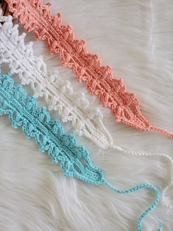 Close-up of aqua, white, and coral crochet headbands showing the delicate lacy stitch pattern and ties.