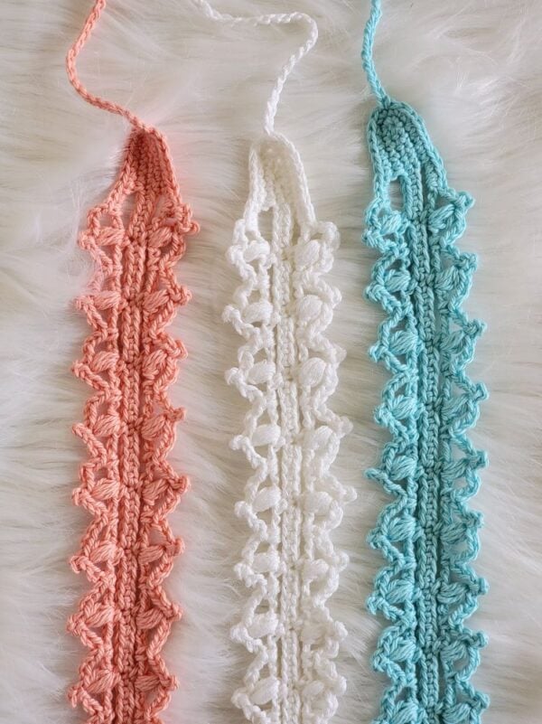 : Coral, white, and aqua lacy crochet headbands laid vertically on a white faux fur background.