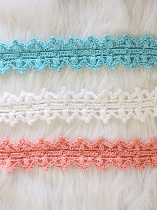 Aqua, white, and coral crochet headbands laid horizontally to show the repeating lacy stitch pattern.