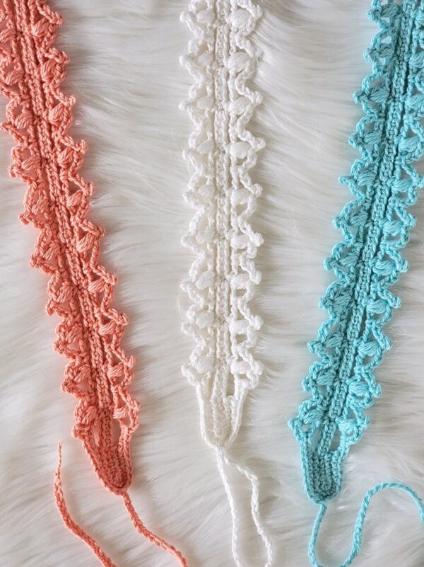 Close-up of three lacy crochet headbands in coral, white, and aqua showing the textured stitch design.