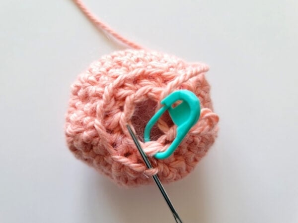 Yarn needle inserted into a small loop at the bottom opening of the stuffed crochet octopus head.
