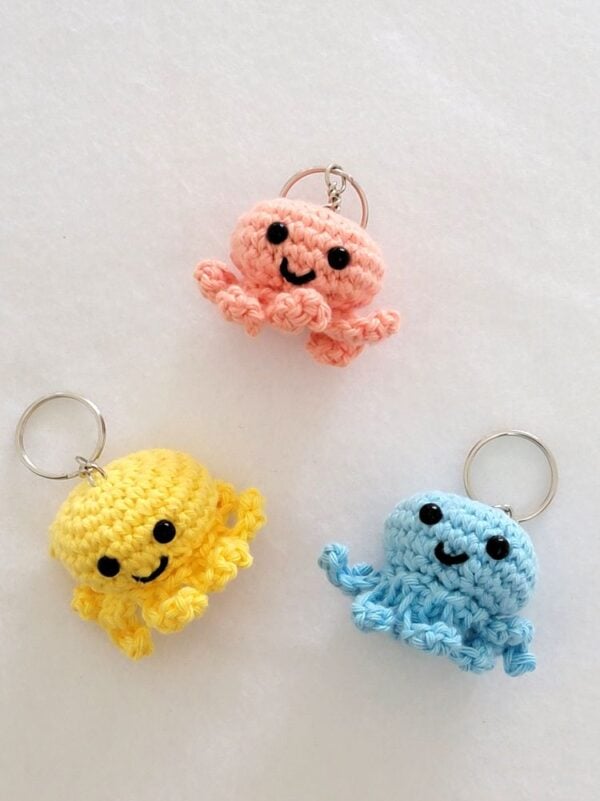 Pink, yellow, and blue crochet octopus keychains with black eyes, embroidered smiles, and curled tentacles.