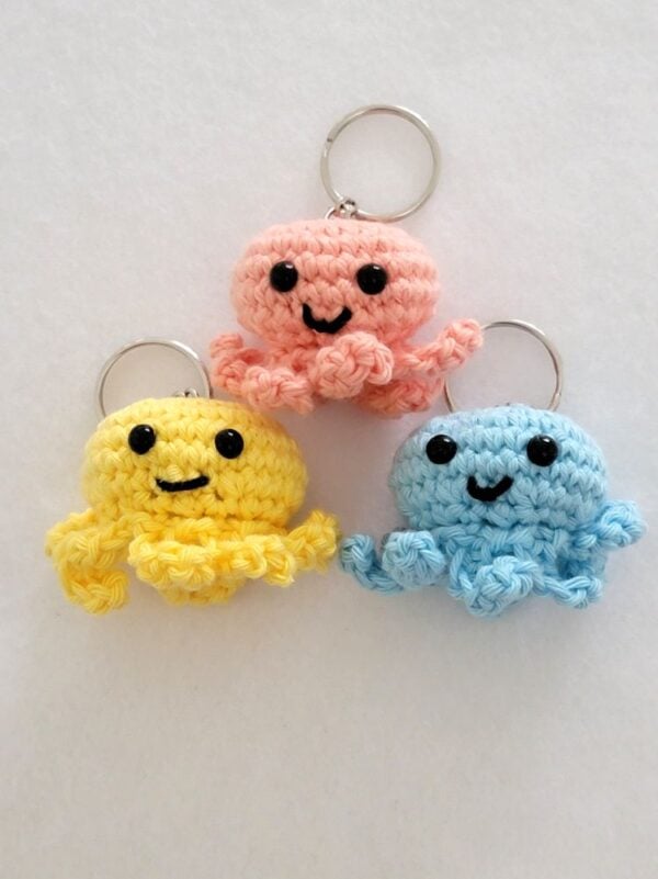 Pink, yellow, and blue crochet octopus keychains arranged vertically on a white background.