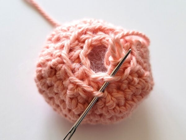 Yarn needle passed through two loops around the bottom opening of the crochet octopus head.