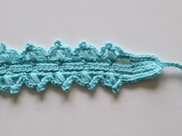 Close-up of the lacy crochet headband showing the completed puff stitch round and tapered end.