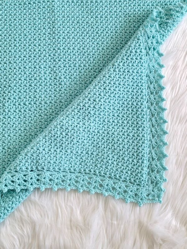 Close-up of a simple aqua crochet baby blanket showing the textured one-row repeat stitch and decorative lace edging.