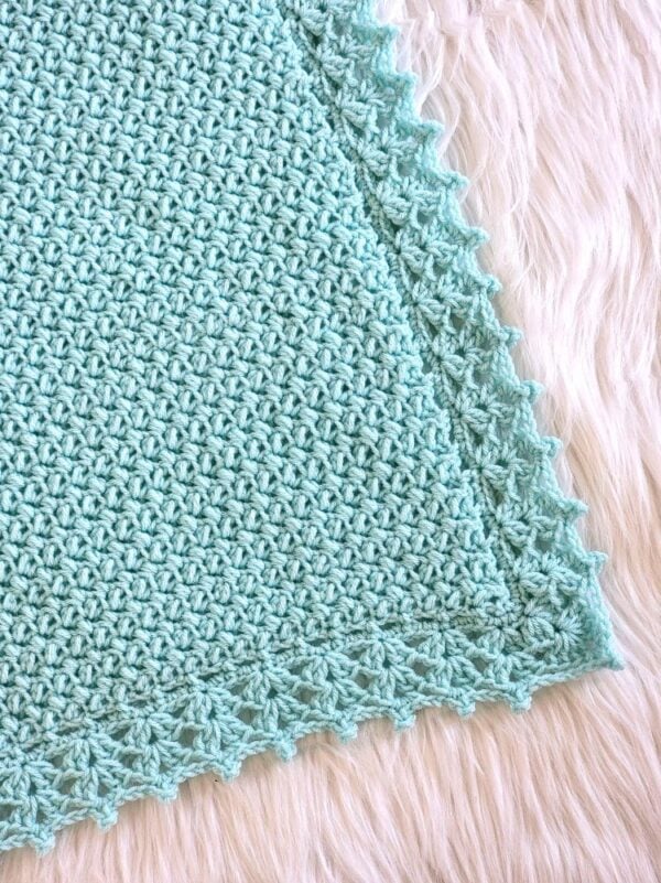 Close-up of the corner of an aqua crochet baby blanket showing the textured stitches and delicate lacy crochet border.