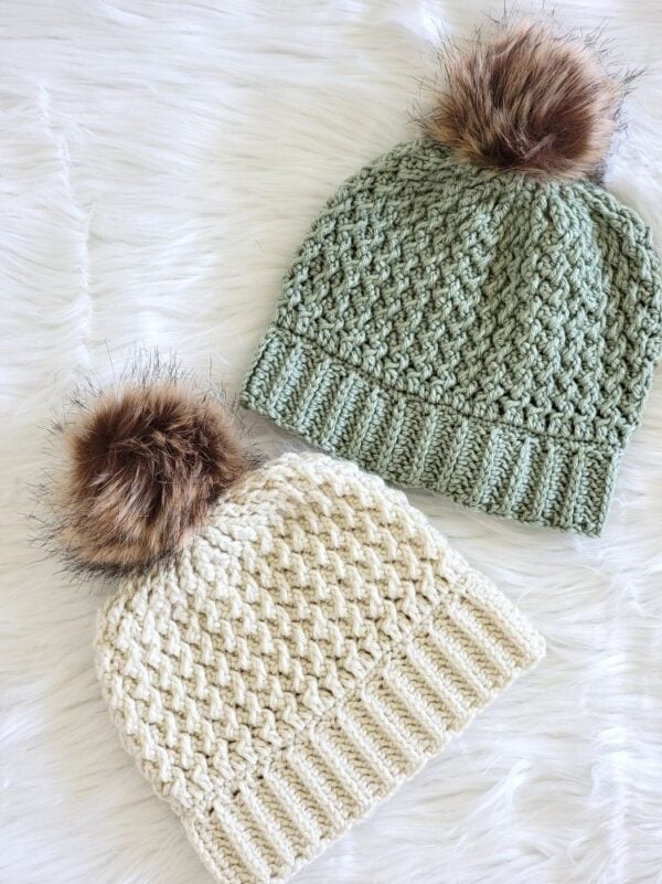 Cream and sage green crochet hats with textured stitch patterns, ribbed brims, and faux fur pom poms.