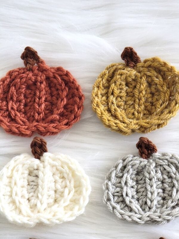 Close-up of four textured crochet pumpkin appliqués with raised stitches and brown stems in beautiful fall colors.