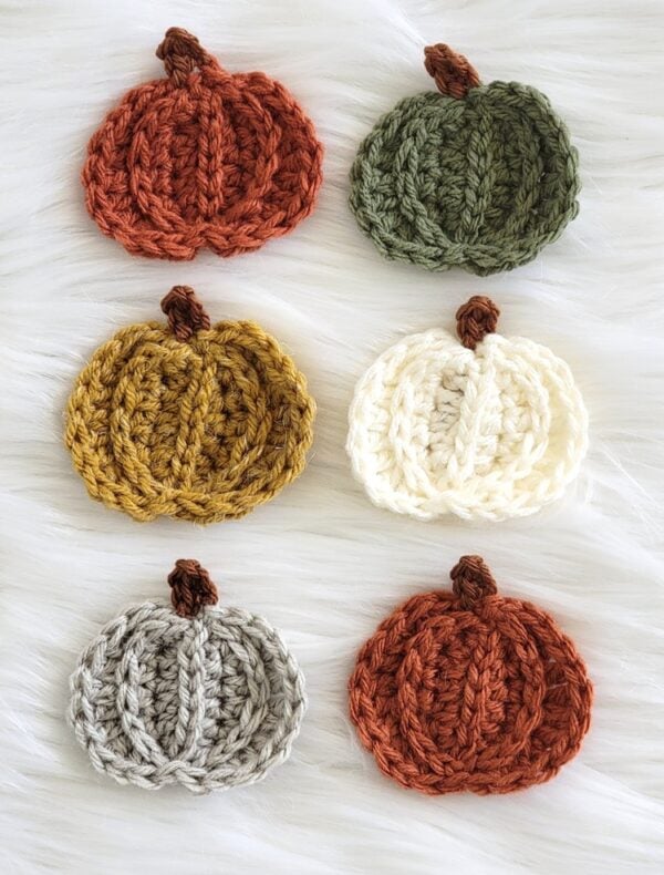 Six small crochet pumpkin appliqués arranged in rows, showing a free fall crochet appliqué pattern in different colors.