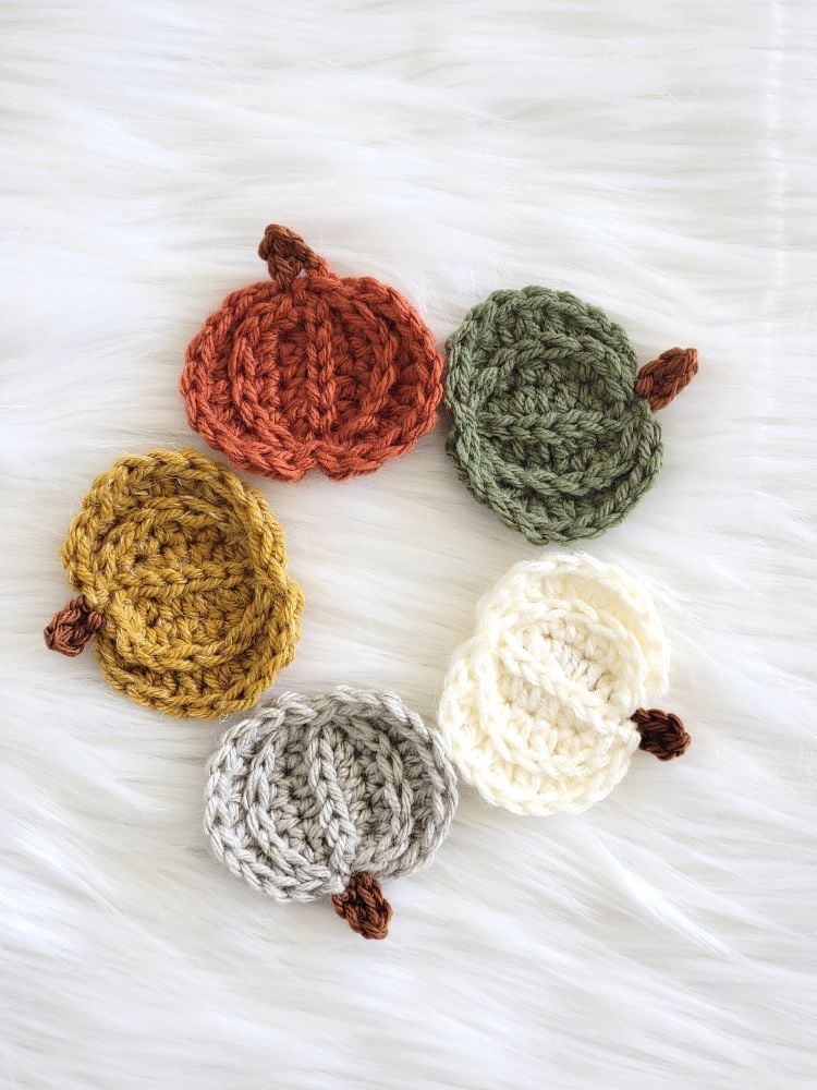 Five mini pumpkin crochet appliqués arranged in a circle, featuring textured stitches and brown yarn stems.