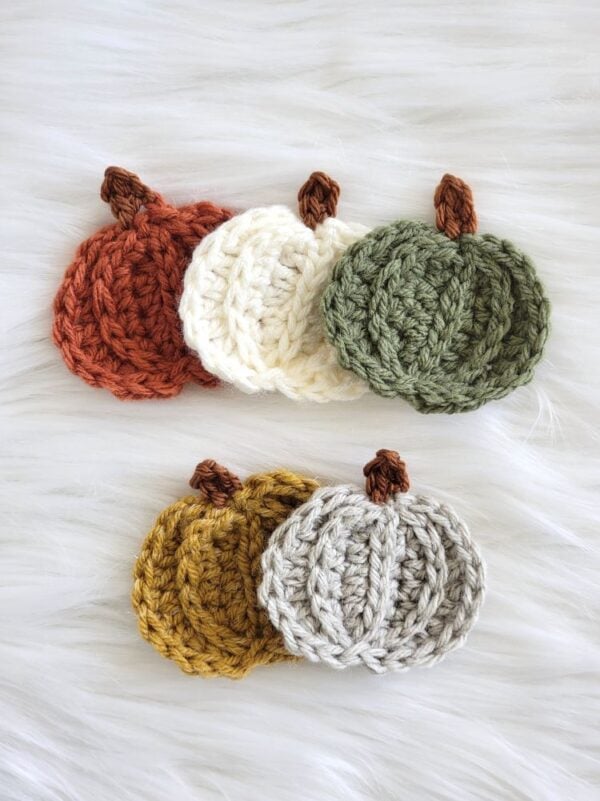 Easy crochet pumpkin appliqués in autumn colors, arranged in two overlapping groups on a white faux fur background.