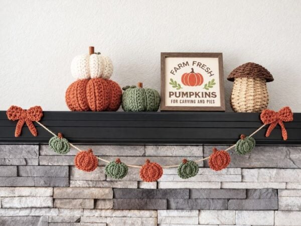 Crochet pumpkin garland with orange and green pumpkins decorating a fall fireplace mantel.