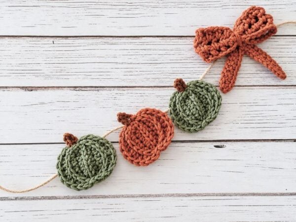 Close-up of green and orange crochet pumpkins with a matching bow on a twine garland.