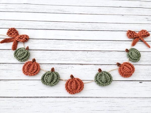 Crochet pumpkin garland with alternating green and orange pumpkins and bows at both ends.