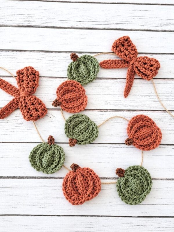 Handmade fall pumpkin garland with orange and green crochet pumpkins arranged on a white wooden background.