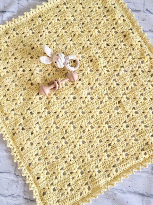 Handmade yellow floral crochet baby blanket displayed flat with a crocheted bunny rattle and wooden baby toy.