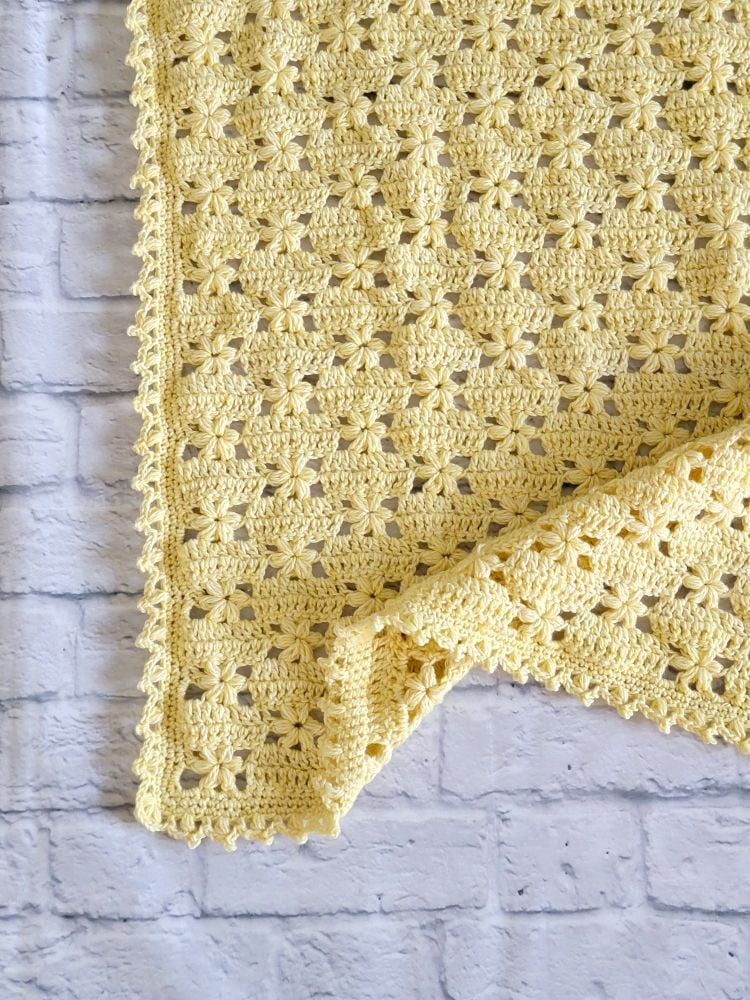Close-up of a yellow crochet flower blanket showing rows of puff stitch flowers and a puff stitch scalloped border.