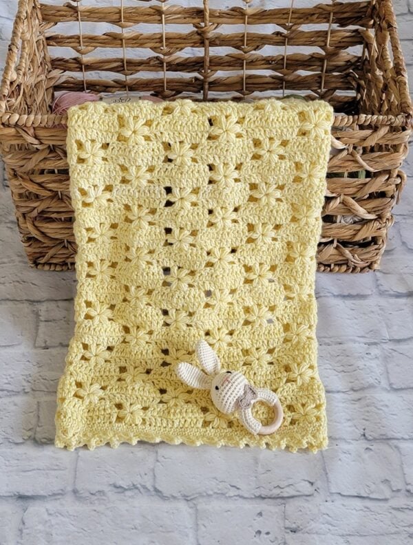 Yellow flower stitch crochet baby blanket hanging over a woven basket, showing the textured floral pattern and decorative border.