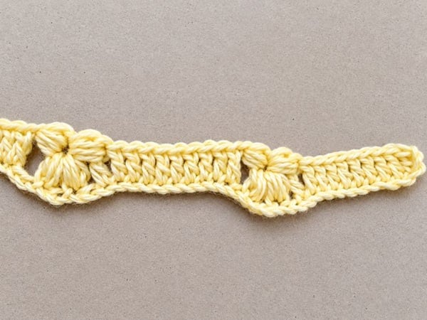 First row of a crochet pattern for a flower baby blanket, showing yellow half puff stitch flowers separated by double crochet stitches.