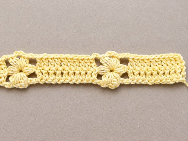 First row of a crochet pattern for a yellow flower baby blanket, showing complete puff stitch flowers separated by double crochet stitches.