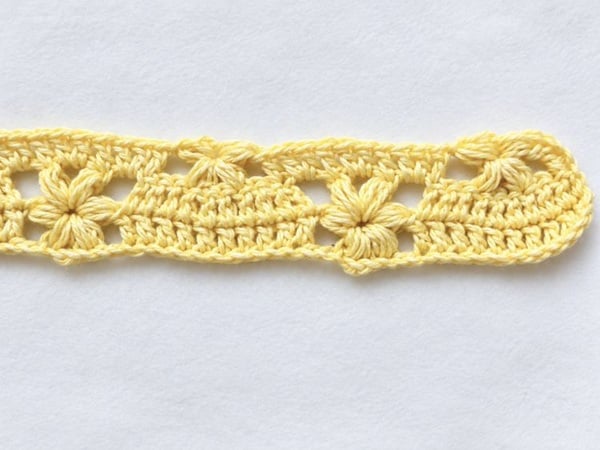 Third row of a crochet pattern for a flower baby blanket, showing yellow half puff stitch flowers separated by double crochet stitches.