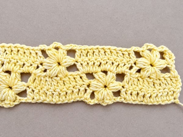Row 4 of yellow flower blanket completed showing 3 full puff stitch flowers