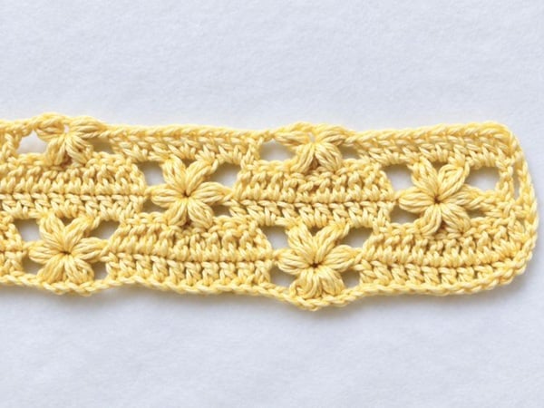Fifth row of the flower baby blanket crochet pattern showing a repeating design of raised flowers and double crochet stitches.