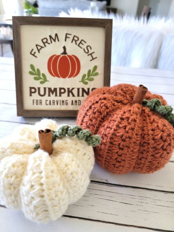 Cream and orange crochet pumpkins with cinnamon stick stems and curly green vines displayed beside a farmhouse pumpkin sign.