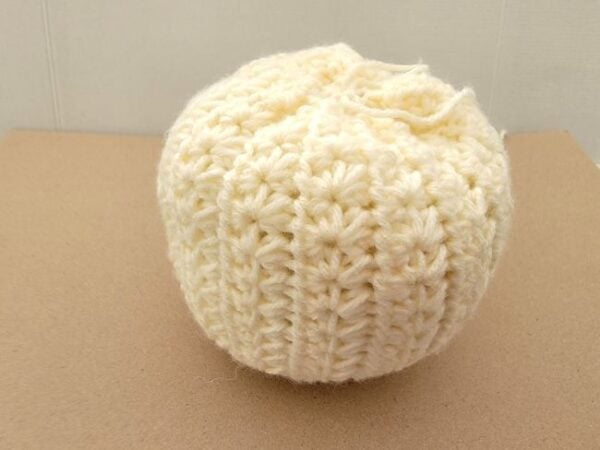 Tall cream crochet pumpkin before the yarn is added to divide it into rounded segments.