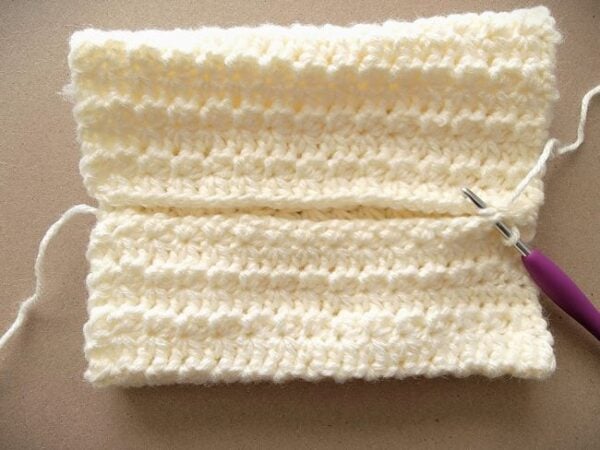 Crocheted pumpkin body folded with the two edges being seamed together to form a tube.