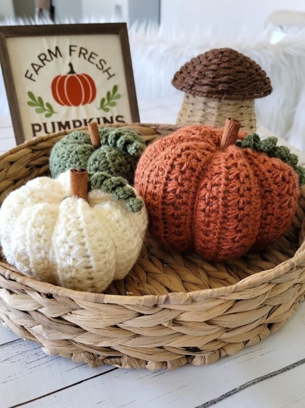 Three star stitch crochet pumpkins in orange, cream, and sage green displayed in a woven basket with fall decor.